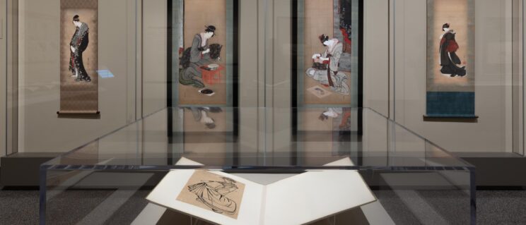 a book on display in front of several Japanese hanging scrolls on a wall